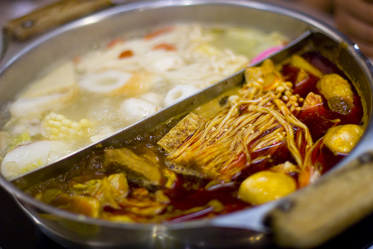 cierre de una olla caliente china dividida en dos mitades por una pieza de metal, llena de dos tipos de caldo, una mitad roja y picante, la otra mitad es transparente