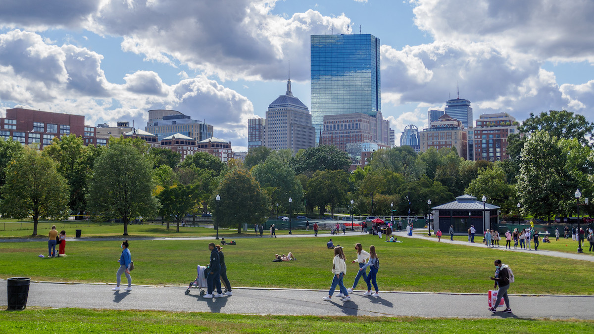 Plano general de Boston Common, la gente camina por la acera, algunas personas están tumbadas en la hierba, rascacielos en el fondo
