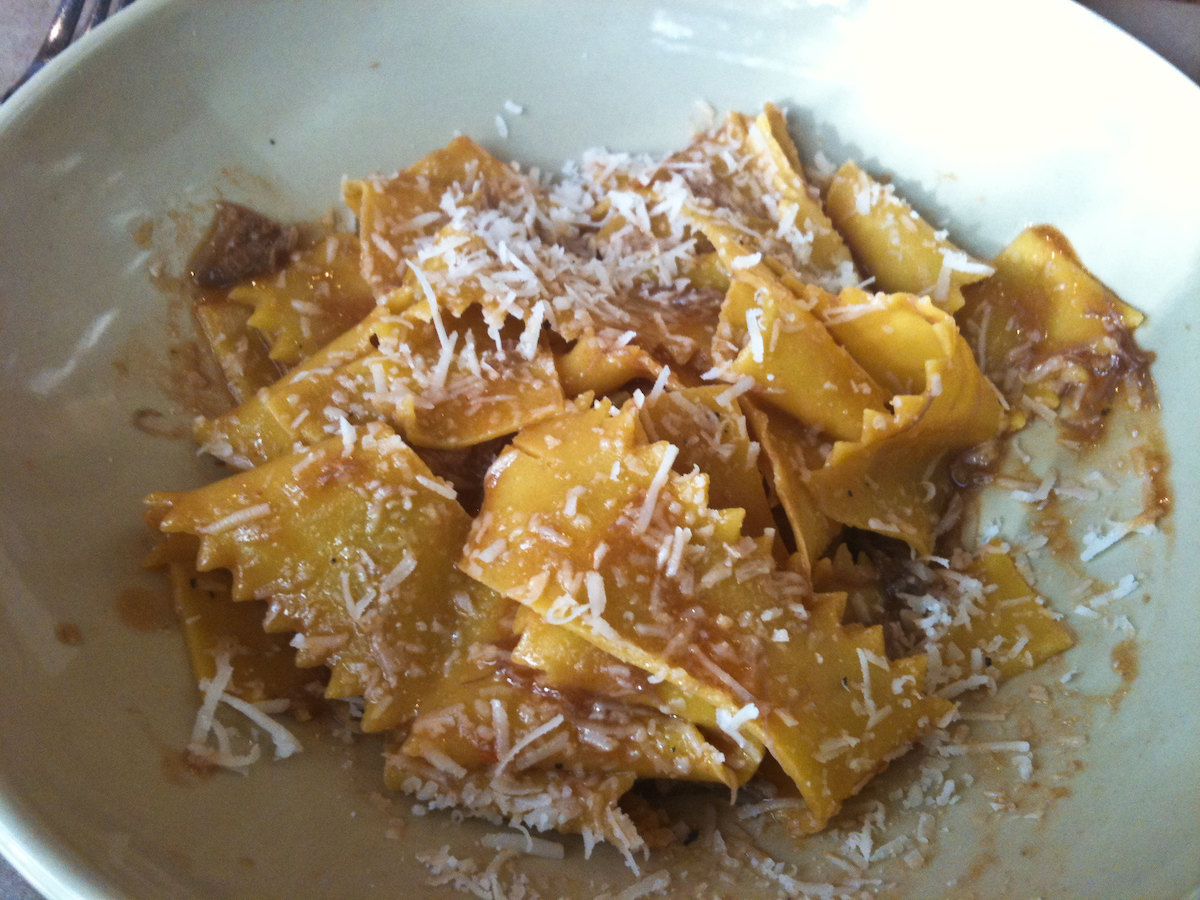 Primer plano de un tazón blanco lleno de pasta papardelle plana y ancha hecha a mano con ragú de cordero cubierto con queso blanco rallado