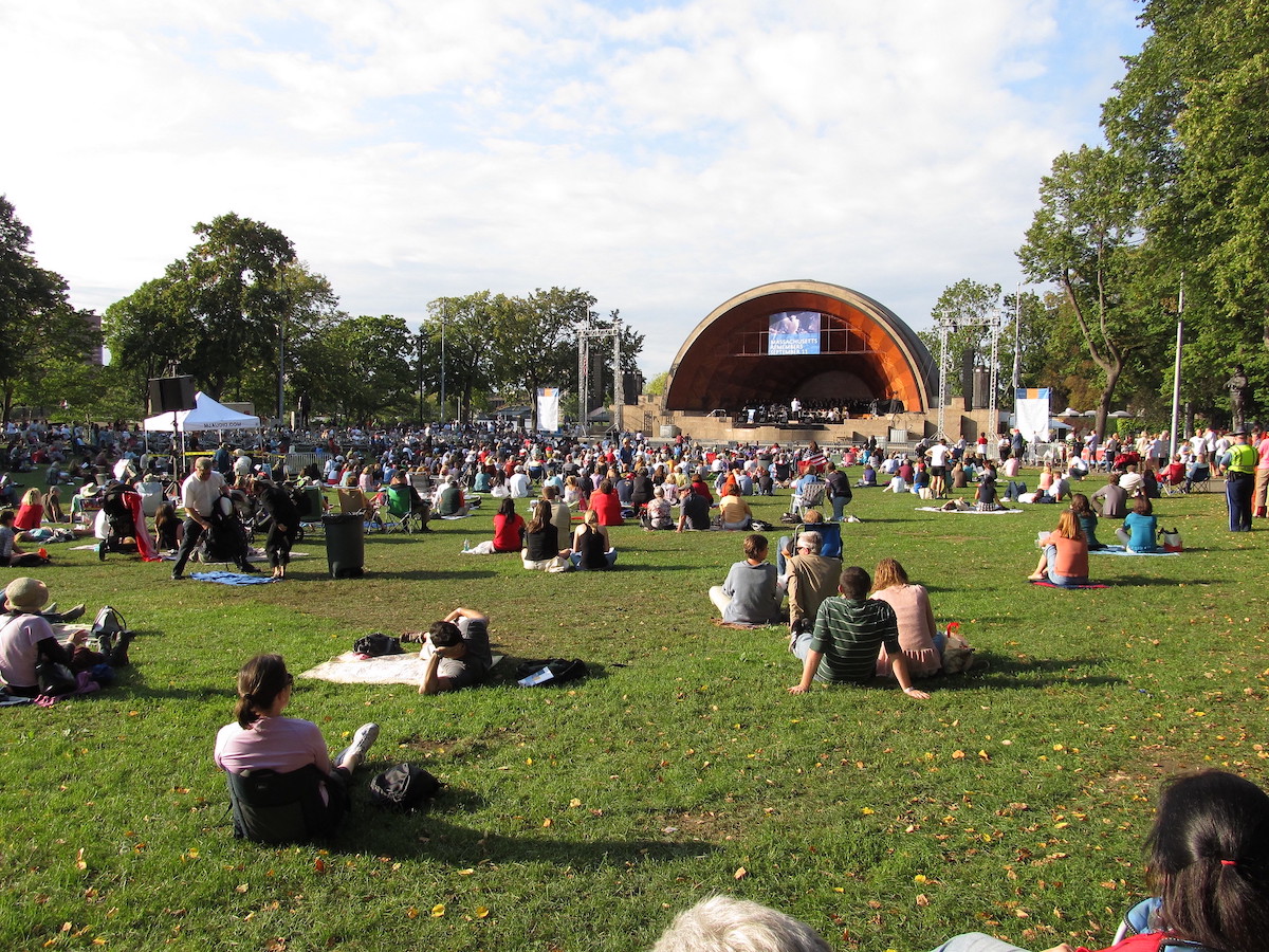 La gente se sienta en un césped verde con Hatch Shell en Boston al fondo