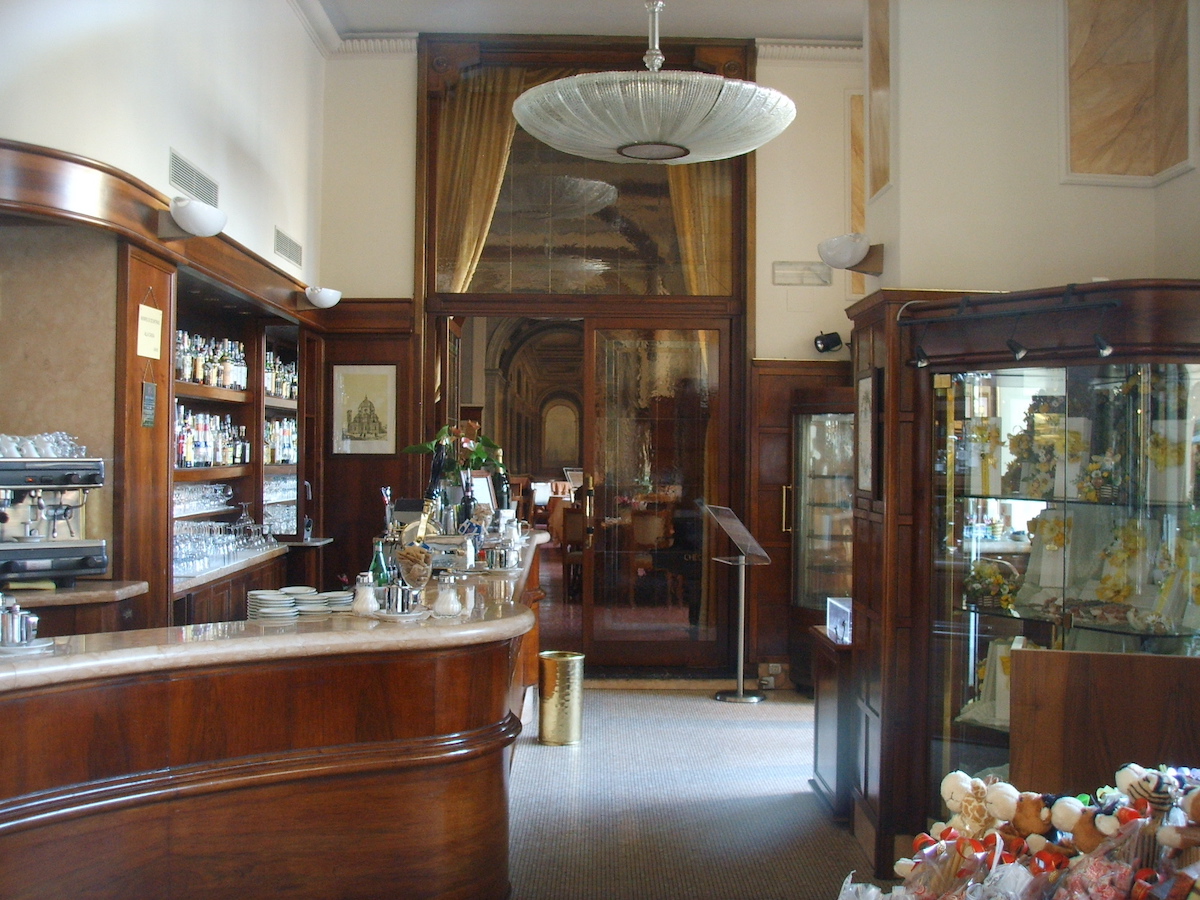 Interior de un café histórico en Florencia, Italia, con bar envolvente, detalles de madera oscura y lámparas de los años 20