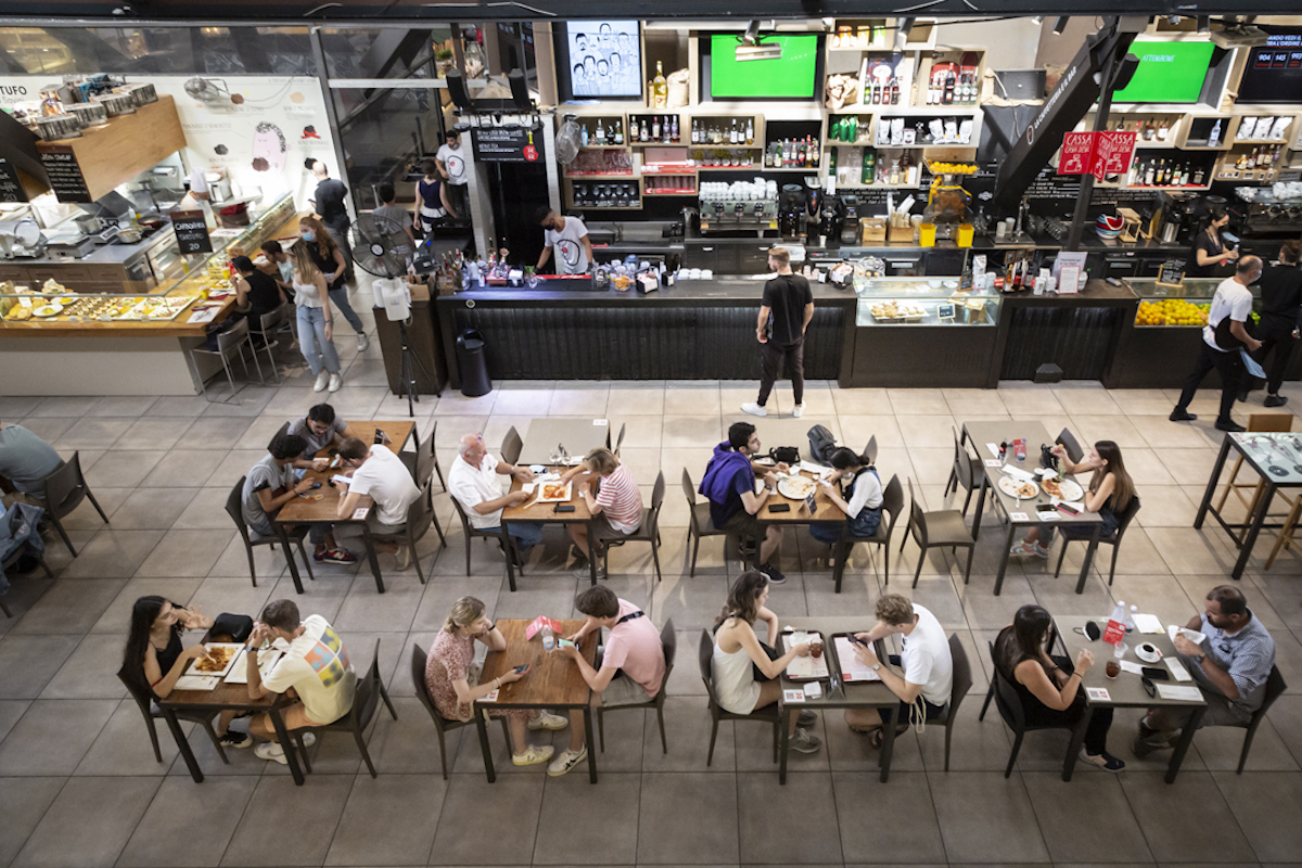 Fotografía cenital de personas comiendo en mesas dentro de un mercado de alimentos