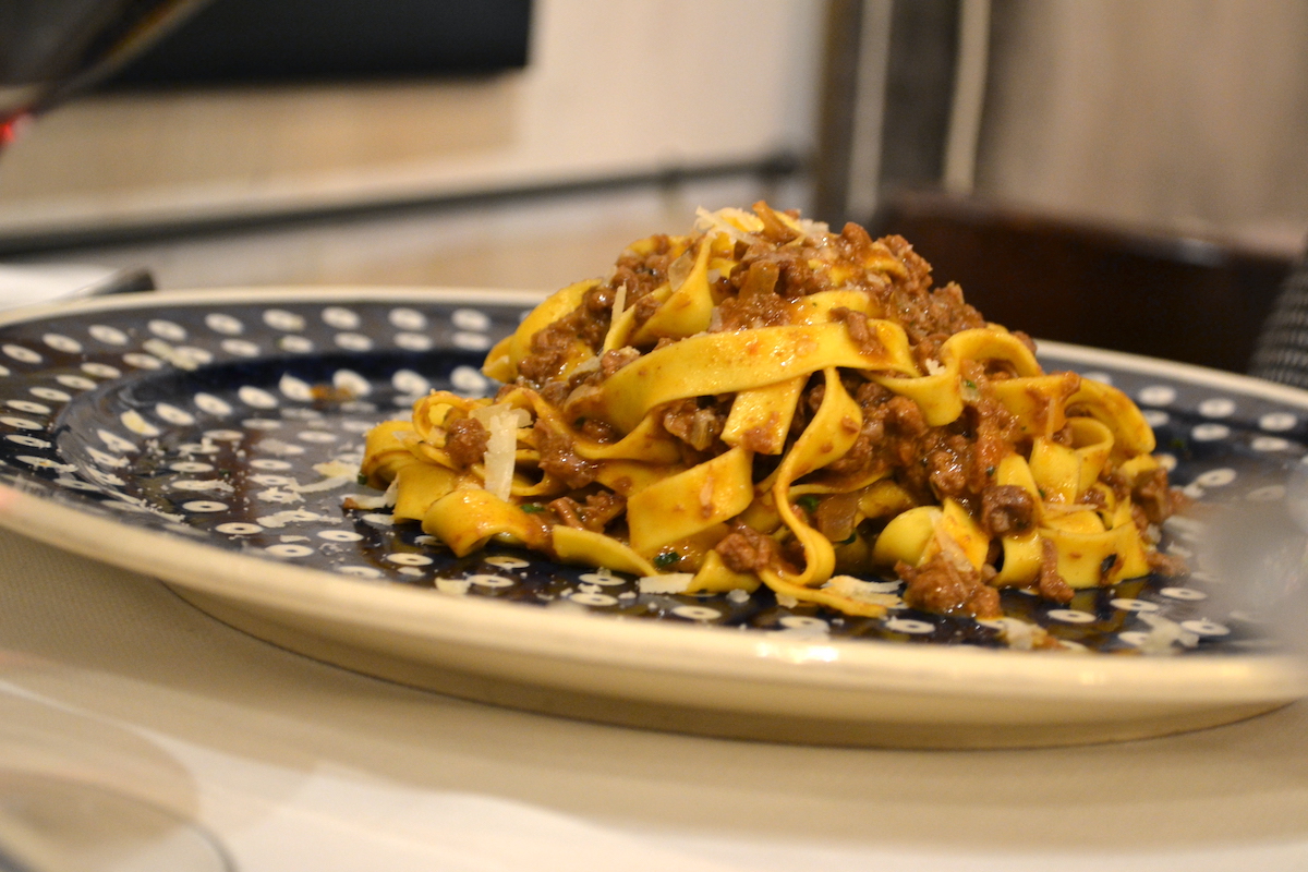 Fideos anchos de pasta servidos con ragú de jabalí en un plato azul y blanco
