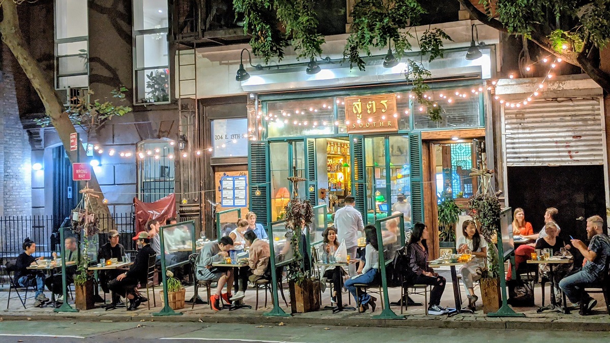 Los clientes comen afuera en mesas en un restaurante en la ciudad de Nueva York con luces