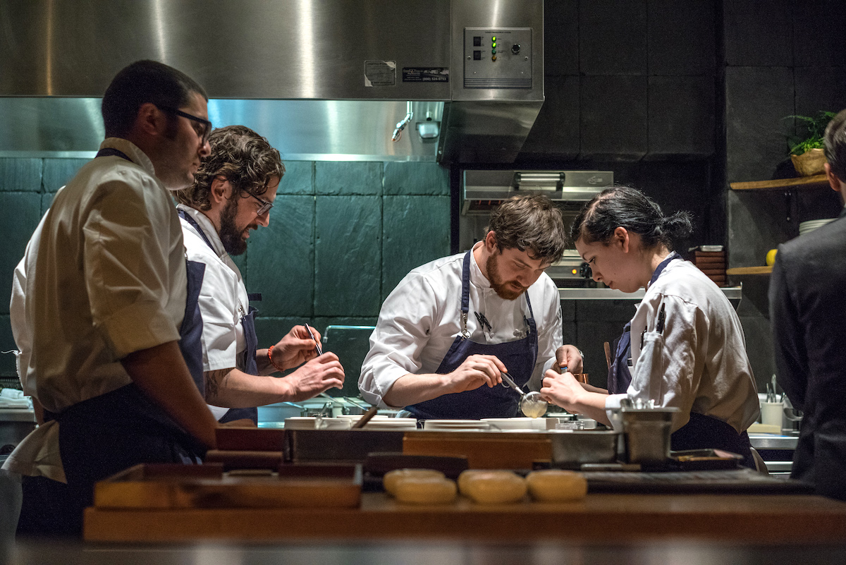 Cuatro chefs con delantales negros trabajan en una cocina abierta