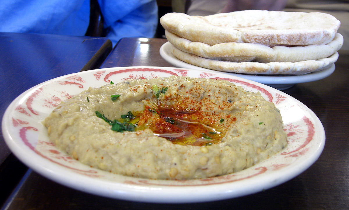 Baba ghanoush servido en un plato de cerámica rojo y blanco con una pila de pitas al fondo.