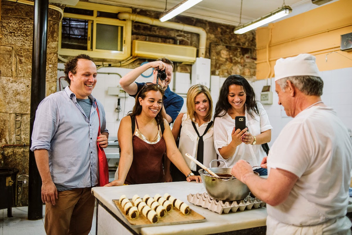 Un grupo de personas viendo a un panadero sumergir un pastel en chocolate.