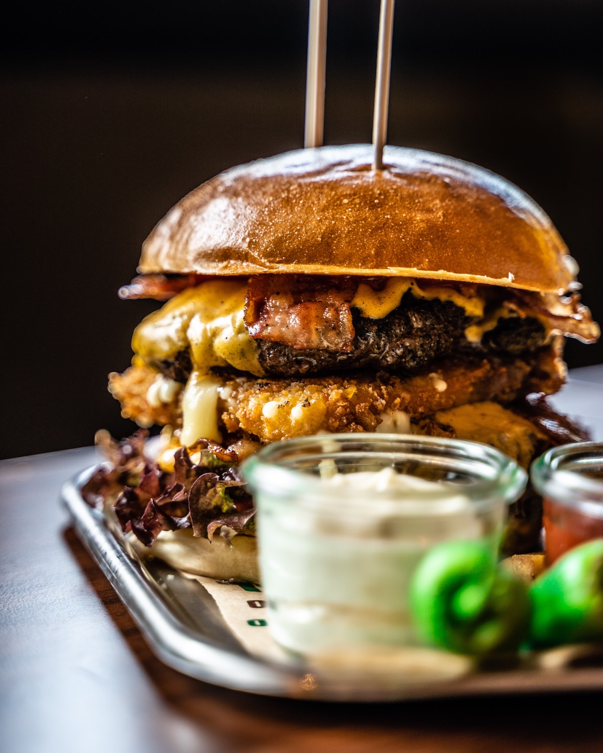 Una hamburguesa con queso en una bandeja con un pequeño recipiente de salsa blanca delante.