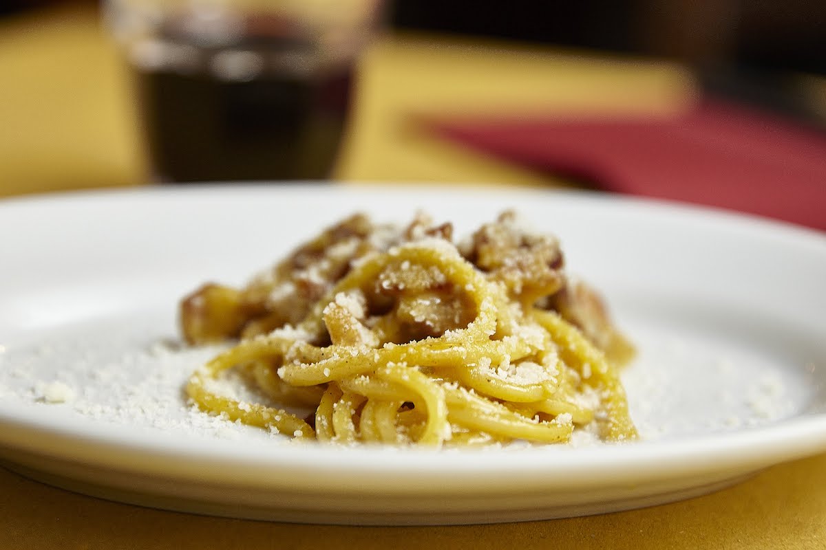 Spaghetti carbonara servido en un plato blanco con una copa de vino tinto todavía en el fondo