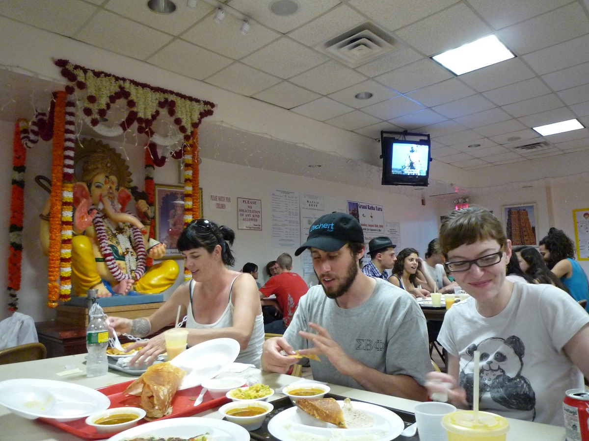 Ambiente de cafetería dentro de un templo hindú con cuatro amigos comiendo en un ambiente sencillo