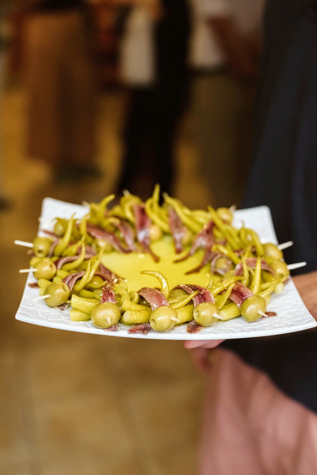 Coloque las brochetas de aceitunas, las anchoas y la pimienta en un plato cuadrado alrededor del aceite de oliva.