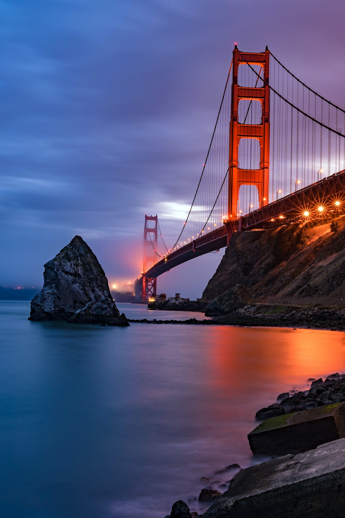 El puente Golden Gate al atardecer con niebla rodando y las luces reflejándose en la bahía de San Francisco.