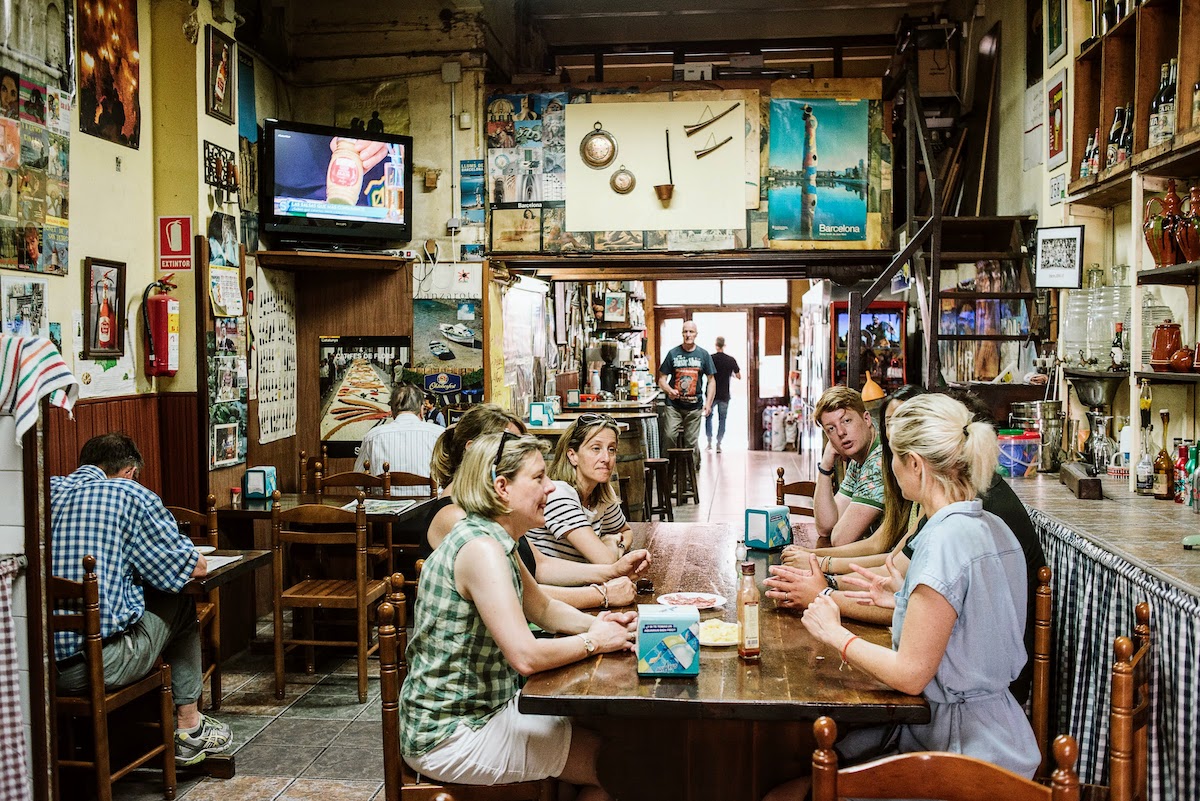 Un grupo de personas sentadas alrededor de una mesa dentro de un extraño bar local en Barcelona.
