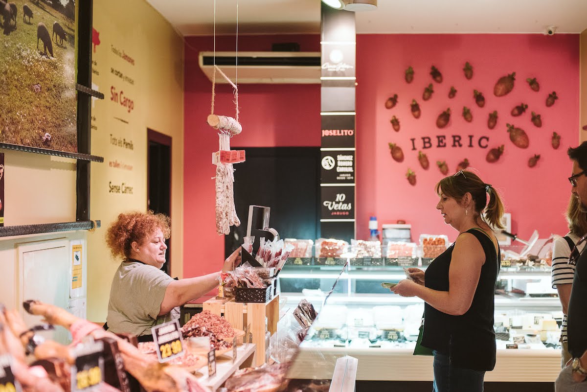 Una mujer compra jamón curado a un vendedor en una tienda de comestibles.