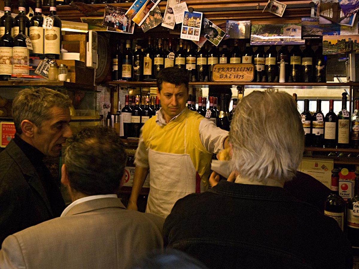 Hombres parados en un bar abarrotado en Florencia mientras un cantinero sirve un sándwich panini.