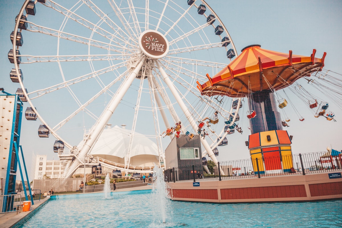 plano general de Navy Pier en Chicago, con una gran rueda de la fortuna blanca en el fondo, un columpio rojo y amarillo a la derecha y una fuente en primer plano