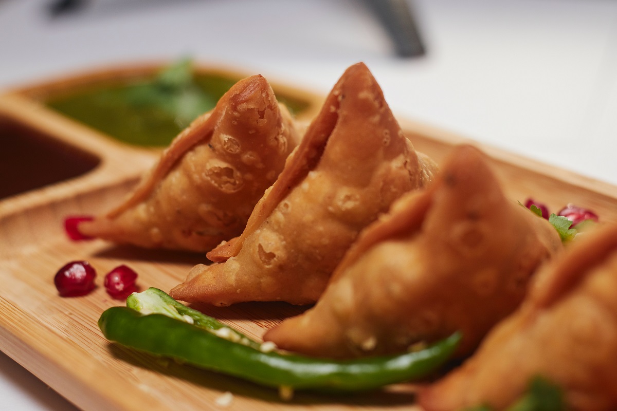 Un plato de madera de tres pequeñas samosas triangulares y pimientos verdes.