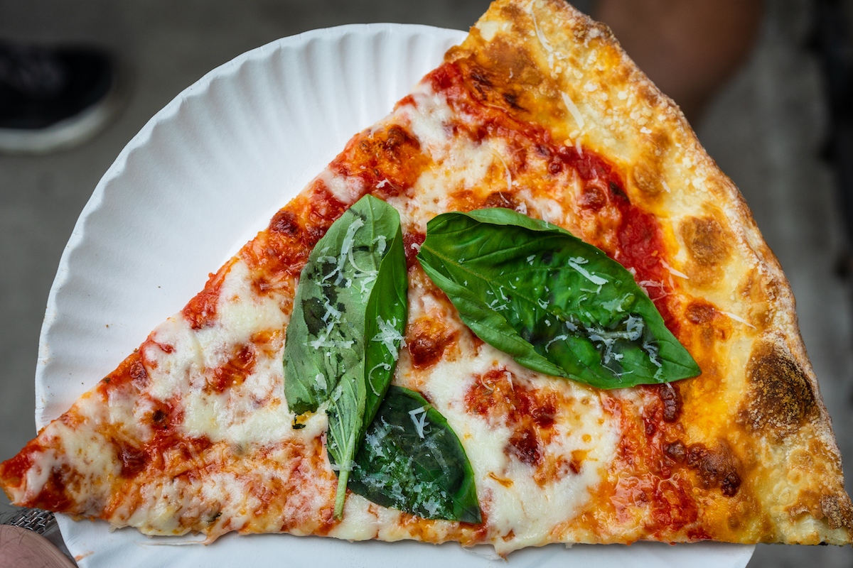 Una rebanada de pizza al estilo de Nueva York cubierta con hojas de albahaca fresca