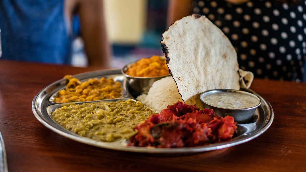 Una bandeja de plata de comida india con mucho curry de colores y pan blanco.