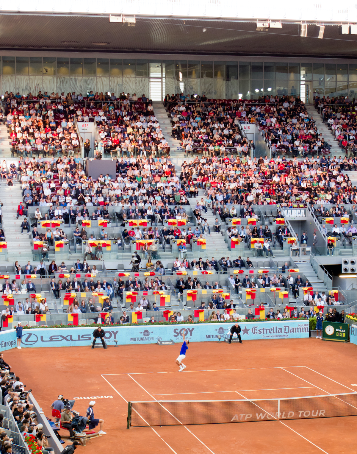 Un partido de tenis que se juega en una cancha de arcilla frente a una multitud.