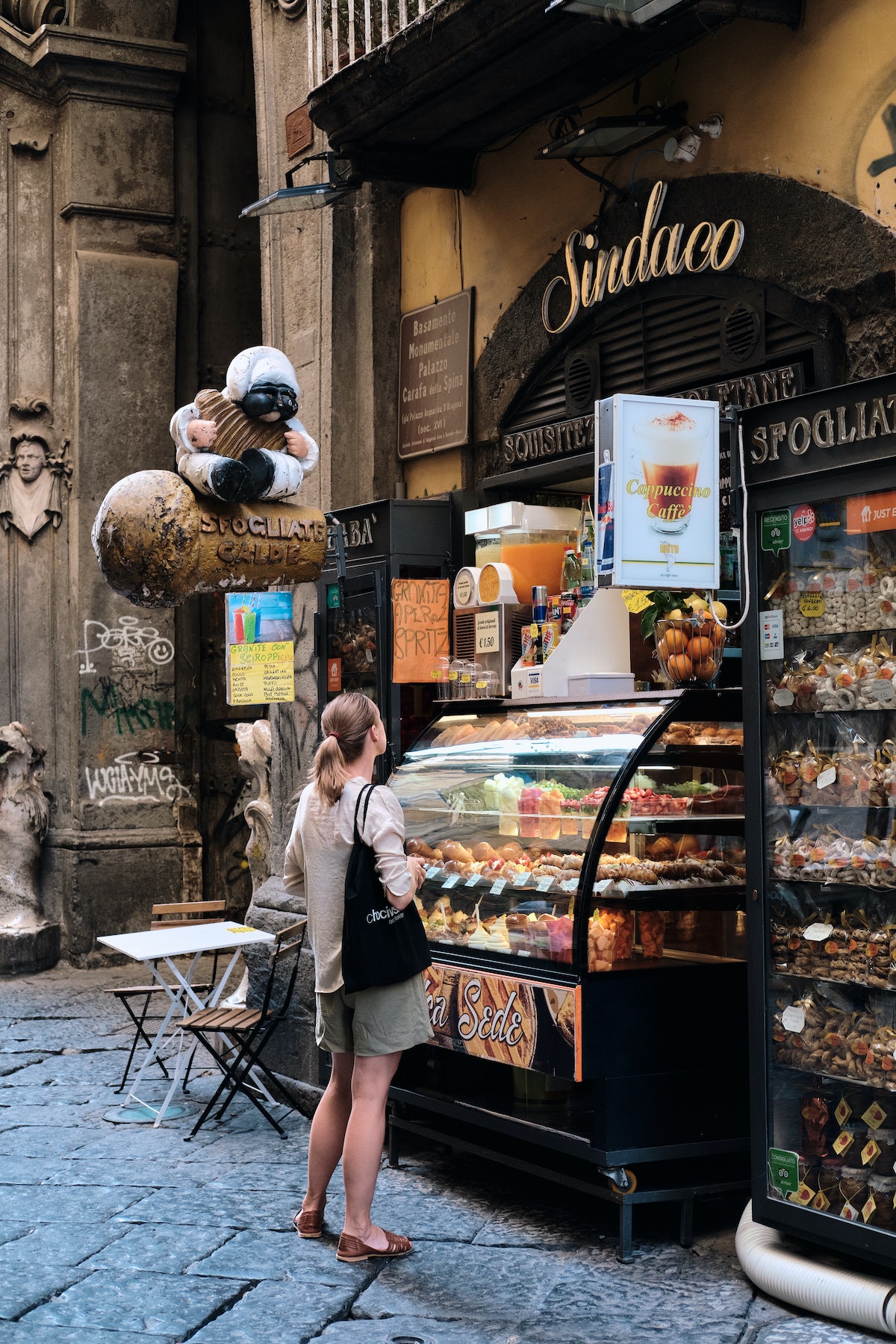 Una mujer se para en la calle y mira dentro de una vitrina de panadería en Nápoles, Italia.