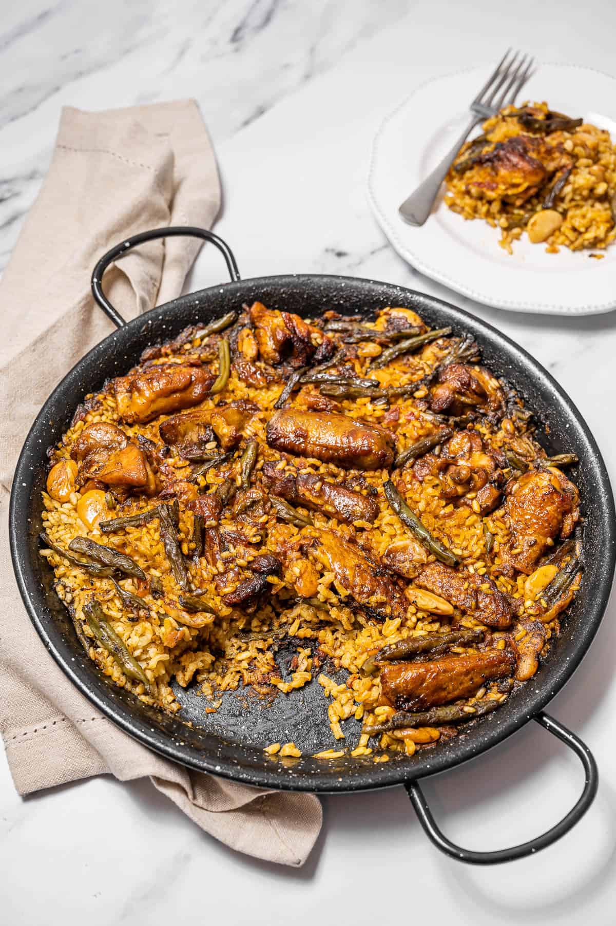 Una cacerola grande de paella valenciana con una porción plateada detrás.