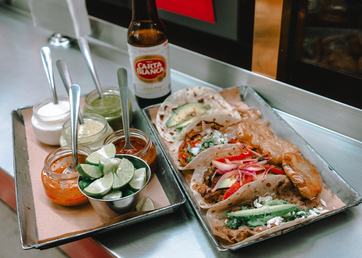 Una bandeja de tacos callejeros con limas, salsas y cerveza