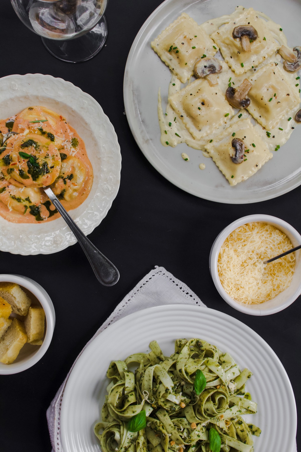 Varios platos de pasta - espaguetis, pesto, tortellini - en una mesa de restaurante con queso.