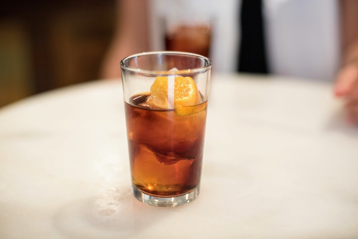 Un vasito de vermut rojo con hielo adornado con una naranja.